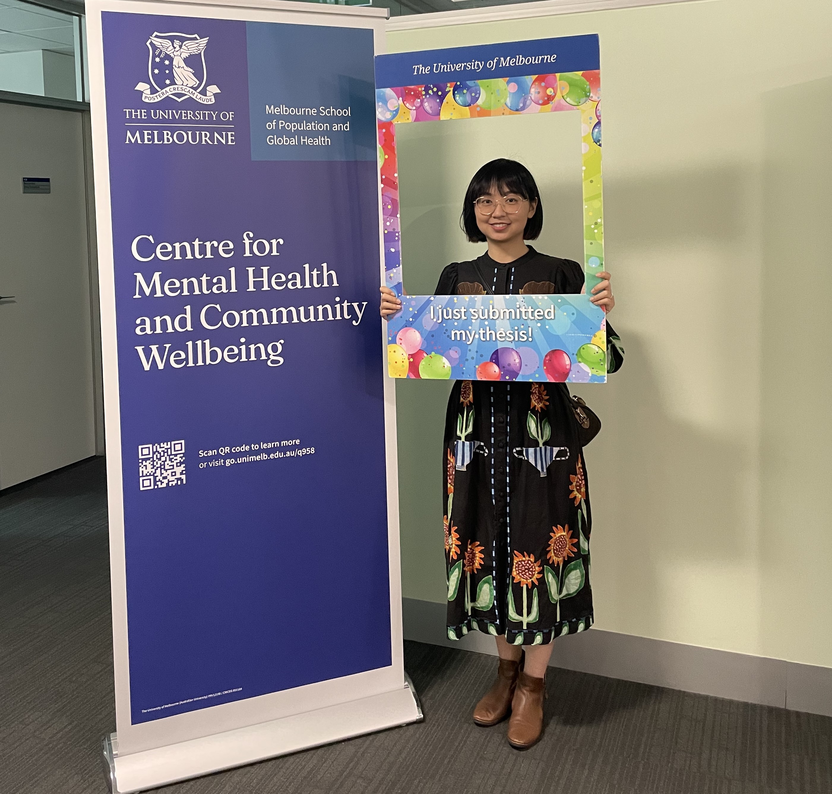 Smiling graduate researcher celebrating their thesis submission with a thesis submission photo frame
